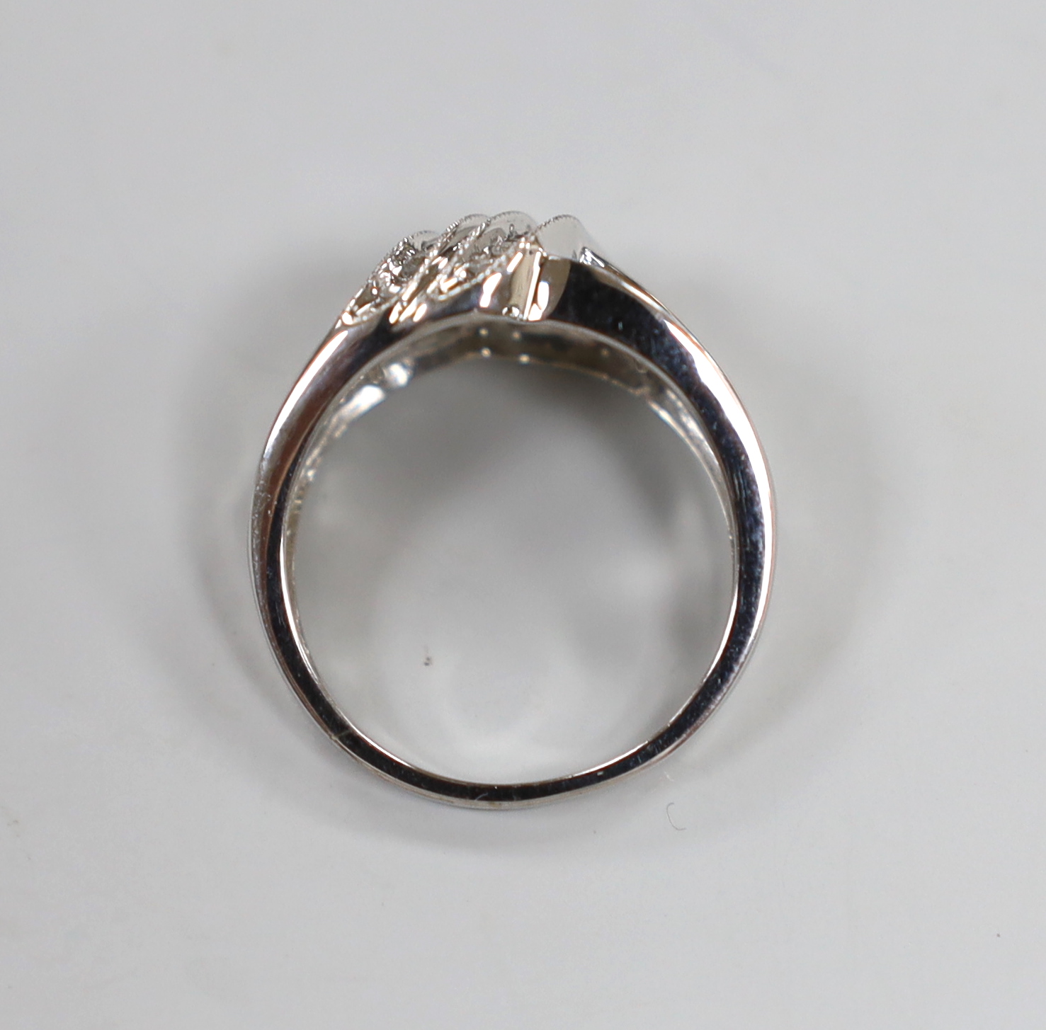 A modern 14k white metal, baguette and diamond chip set crossover cluster ring, size N/O, gross weight 4.5 grams.